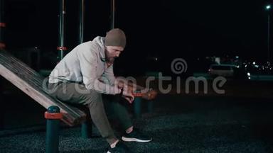 一个人晚上坐在公园里的<strong>运动器材</strong>上，用智能手表